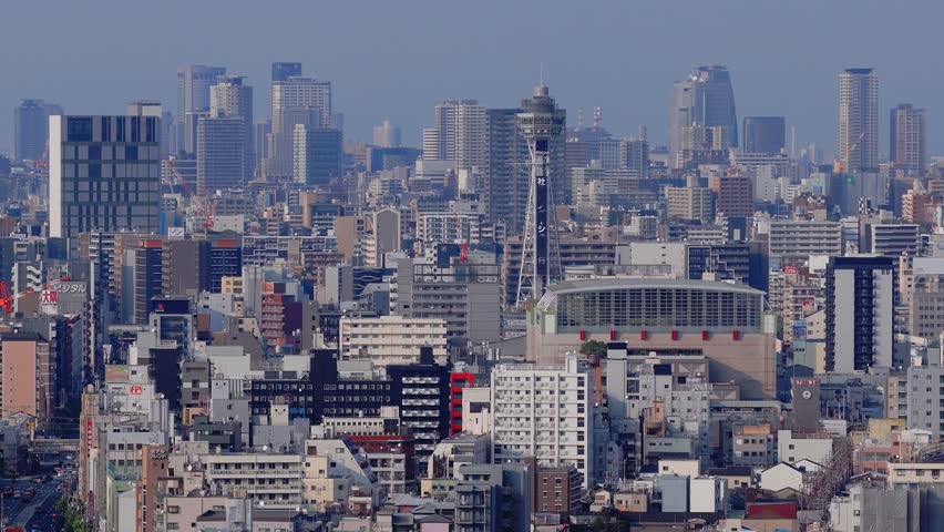 Aerial view of Osaka, Japan, featuring Tsutenkaku Tower, Osaka Castle, and a mix of modern and traditional buildings with gradual panning motion.