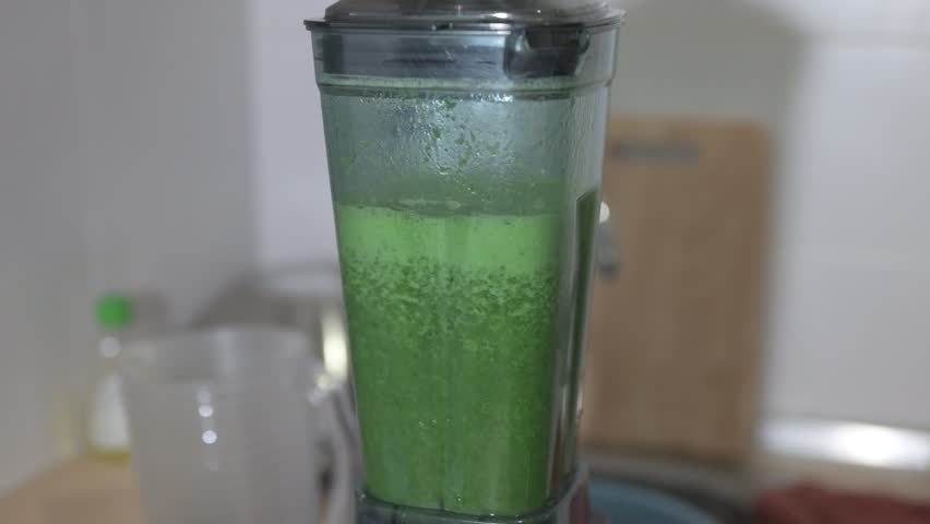 Fresh green smoothie juice prepared in blending machine at home kitchen by woman