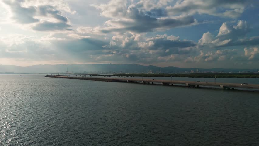Scenic aerial view of a bridge crossing water with cars, city skyline in the background, and dramatic sky with sun rays, perfect for travel and urban projects