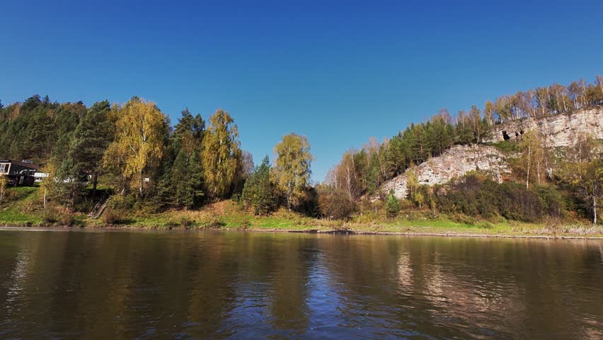 Experience breathtaking views of a winding river flowing through autumn trees and cliffs under a blue sky, perfect for nature projects that highlight outdoor serenity and picturesque landscapes