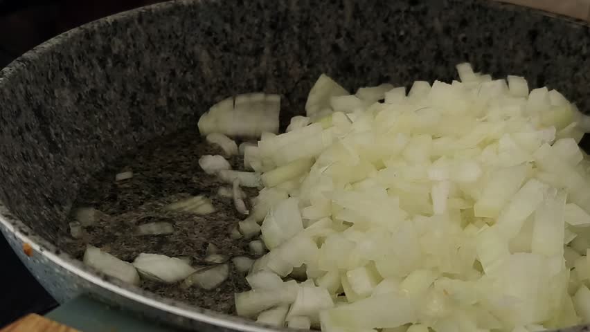 Meal prep process, sauteing chopped onion on a skillet or a frying pan with a wooden spatula. Pouring oil on top. Cooking onions on a gas stovetop. Horizontal, 4K footage