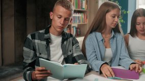 Three teenagers classmates Caucasian pupils students studying together in school doing craft paper art homework with scissor boy reading book cooperation teamwork education at table in library learn - Powered by Shutterstock - Get 15% off with code: PIKWIZARD15