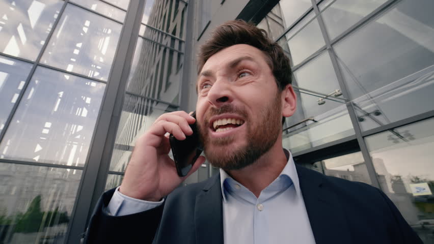 Mad middle-aged Caucasian business man shouting scolding yelling angry to mobile phone conversation arguing problem argument quarrel near office building in city businessman male work failure fury job