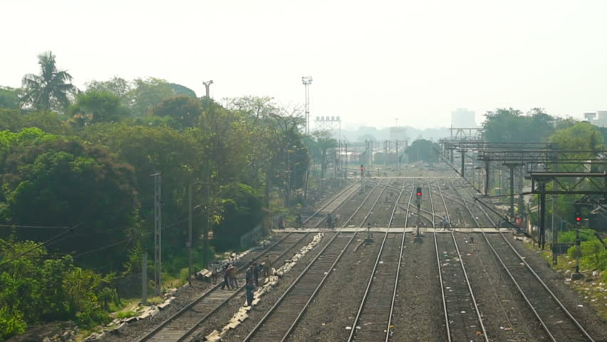 Pedestrians passing through level crossing while a passenger train passes through towards horizon, Howrah, West Bengal, India. Railway workers working on the rail track. Busy view of Indian railway.