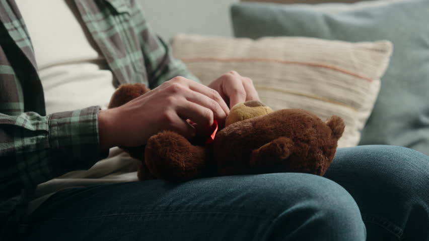 Adult happy Caucasian man indoors holding fluffy toy Teddy Bear preparing gift present for child kid middle-aged carefree male at home positive guy sitting on couch in living room homeowner father