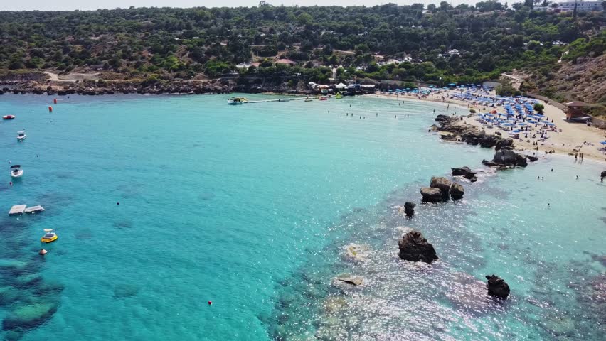 Aerial view of Mediterranean coastline with umbrellas, swimmers and white sand beach. Konnos Beach, Cyprus. Tourist oasis by the azure sea. Mediterranean nature. 
