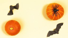 Paper bats fly near orange pumpkins and a black spider. Halloween holiday concept. Greeting card. Bats fly by flapping their wings. Light yellow background. Copy space. Stop motion animation. Flat lay - Powered by Shutterstock - Get 15% off with code: PIKWIZARD15