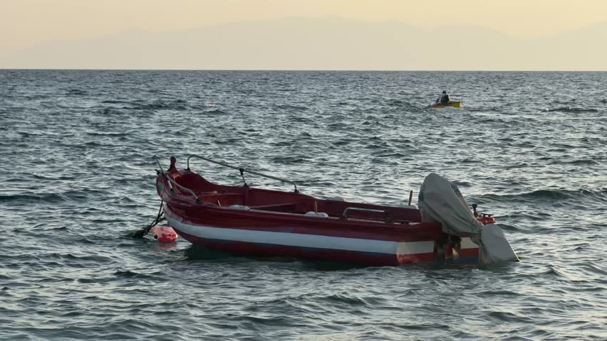 Fishing boat anchored in the sea. The boat rocks on the sea waves. A man on a motorboat sails through the sea. Aegean Sea in Greece, Halkidiki