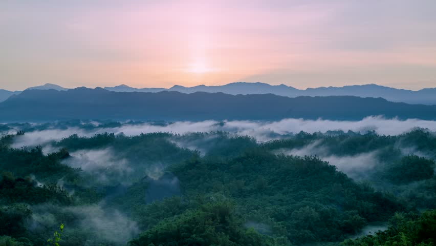 Beautiful early autumn sunrise at Erliao, Zuozhen, Tainan, Taiwan. Golden sun rises over layered mountains with morning fog rolling through lush green forest.