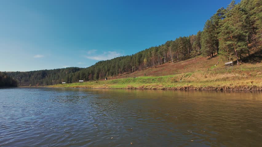 A stunning view of a serene river flowing next to vibrant green fields and forested hills on a sunny day, perfect for nature lovers and outdoor enthusiasts who cherish picturesque landscapes