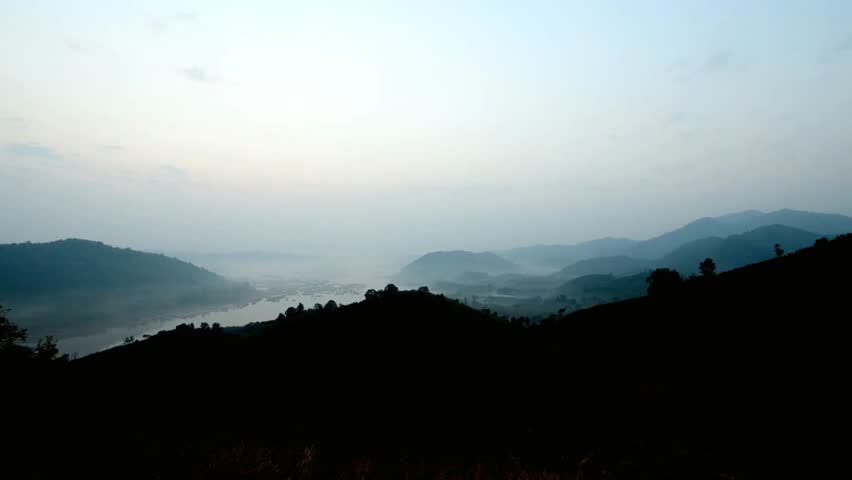 Misty mountains and a river create a scenic landscape at dawn