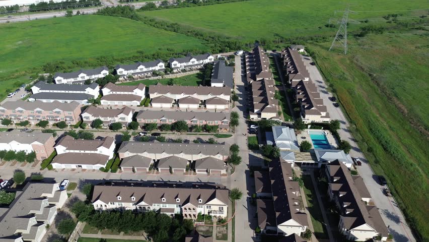 Apartment townhome grid with swimming pool, bordered by grassy vacant land, transmission tower, featuring suburban housing, infrastructure adjacency, and zoning transition in Cypress Water, TX. USA