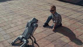 Young boy in sunglasses sitting on a paved area watching an innovative robot dog stand up - Powered by Shutterstock - Get 15% off with code: PIKWIZARD15