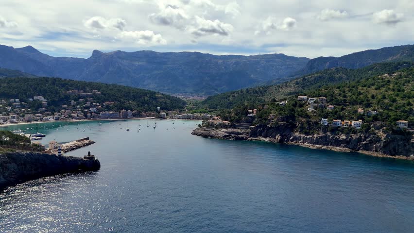 Panoramic coastal landscape of Mallorca featuring lighthouse, blue sea, yachts, marina and surrounding mountains. Ideal for vacation, travel and Mediterranean projects.