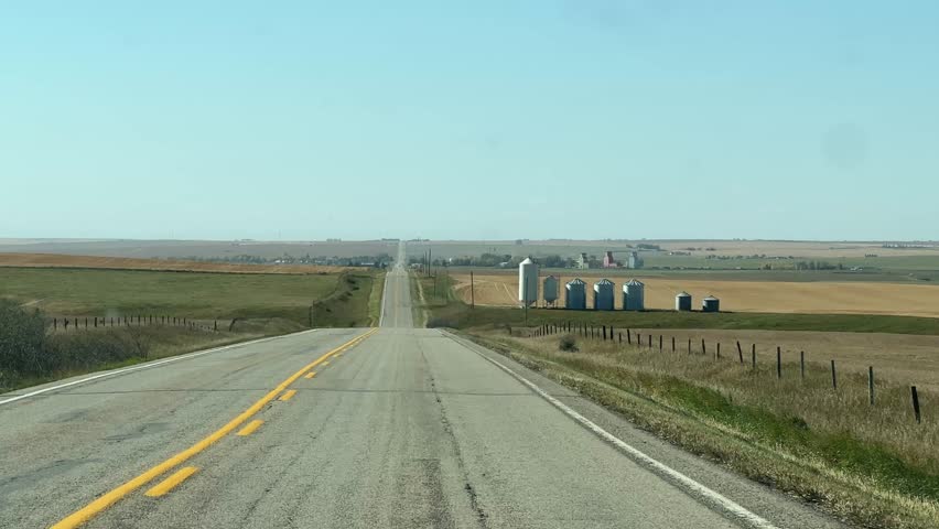 Driving on a rural highway in rural Alberta during daylight with open farmland, clear skies, and scenic prairie landscape, capturing the peaceful beauty of travel through the Canadian countryside.