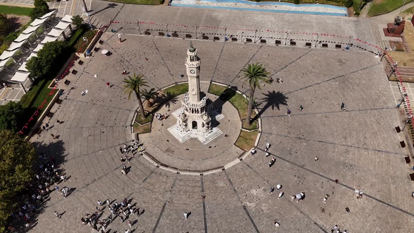 Aerial top view of Izmir Clock Tower in Konak Square, Turkey. Iconic Ottoman landmark surrounded by people, palm trees, and open square near the Aegean Sea