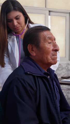 Young physician listening to a senior man's breathing during a medical check up in a hospital clinic. Geriatric care and health examination
