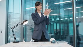Confident Caucasian businesswoman holding wind turbine model while presenting idea in modern glass office. Female professional explaining renewable energy concept near window. Indoors. Standing alone. - Powered by Shutterstock - Get 15% off with code: PIKWIZARD15