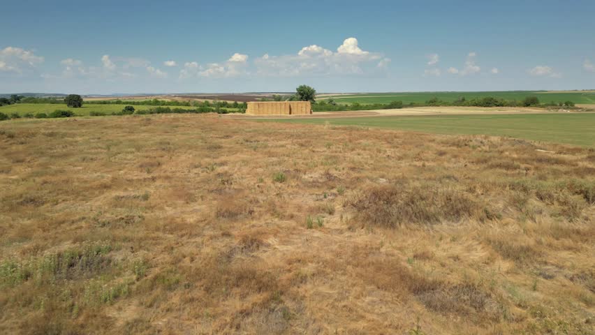 Drone aerial view of stacked rectangular hay bales collected after harvest on farmland, showcasing agricultural production, crop residue management, livestock feeding, and countryside rural environmen