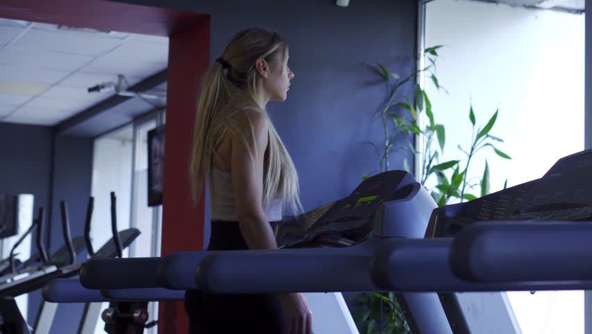 Cardio fitness: Focused female athlete using a modern automated treadmill for brisk walking