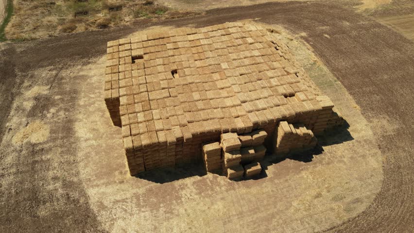 Drone aerial view of stacked rectangular hay bales collected after harvest on farmland, showcasing agricultural production, crop residue management, livestock feeding, and countryside rural environmen
