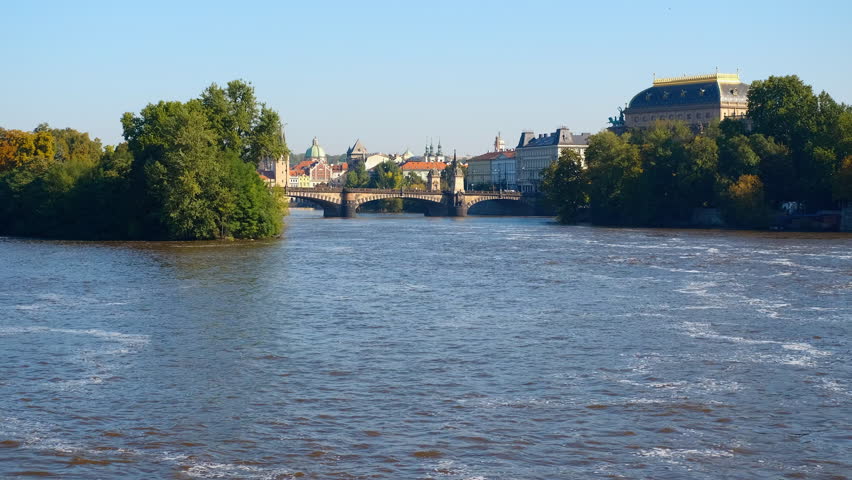 Vltava river flowing under legion bridge in prague. Calm vltava river gently flowing under legion bridge with national theatre rising in background, showcasing serene prague cityscape