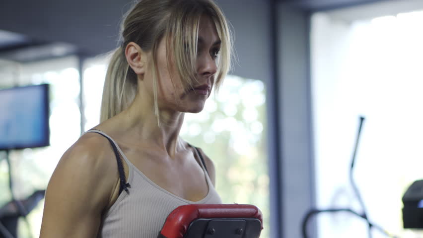 Shoulder Workout: Strong blonde woman doing lateral dumbbell raises on a bench in the fitness club