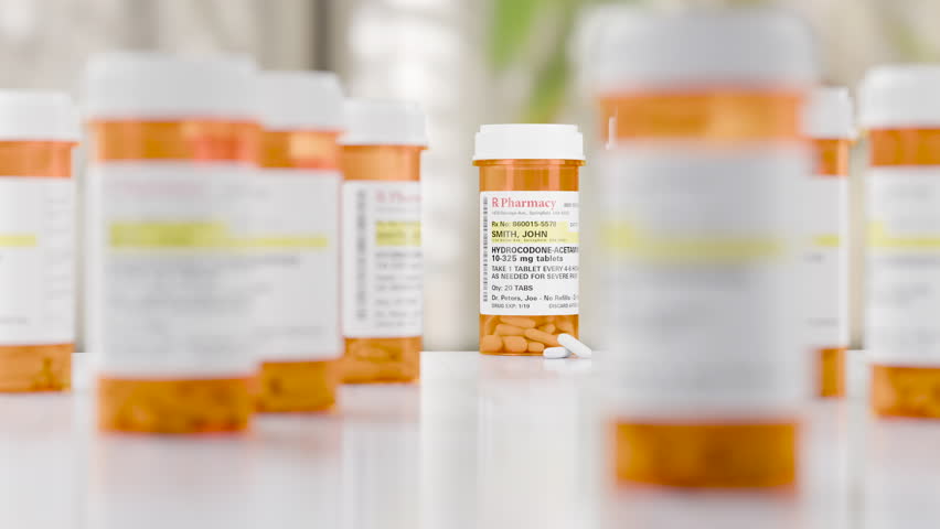 Slow Dolly Camera Movement Hydrocodone Prescription Medicine Bottle and Pills Resting on a Bathroom Countertop. The label is non-proprietary, fictional, made specifically for stock photo industry.