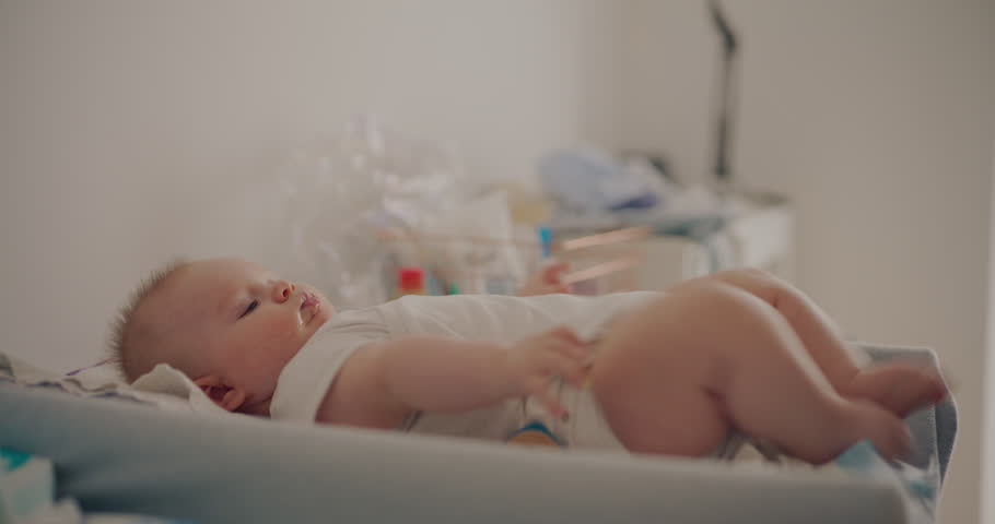 A cute baby boy wiggling and playing on a changing table while waiting for a diaper change.
