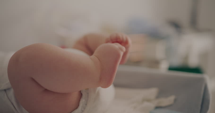 Adorable baby boy lifting his legs joyfully on a changing table, moving his legs with delight.