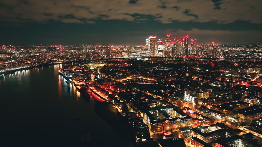 United Kingdom, London: London's illuminated skyline reflecting on the Thames at night, showcasing the vibrant urban landscape and iconic landmarks. Breathtaking aerial view, drone flight panorama