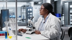 African American scientist focuses on a microscope with tray of samples in modern laboratory. Using observation tool for diagnostics, molecular analysis and discovery. Optics in bioscience. Camera B. - Powered by Shutterstock - Get 15% off with code: PIKWIZARD15