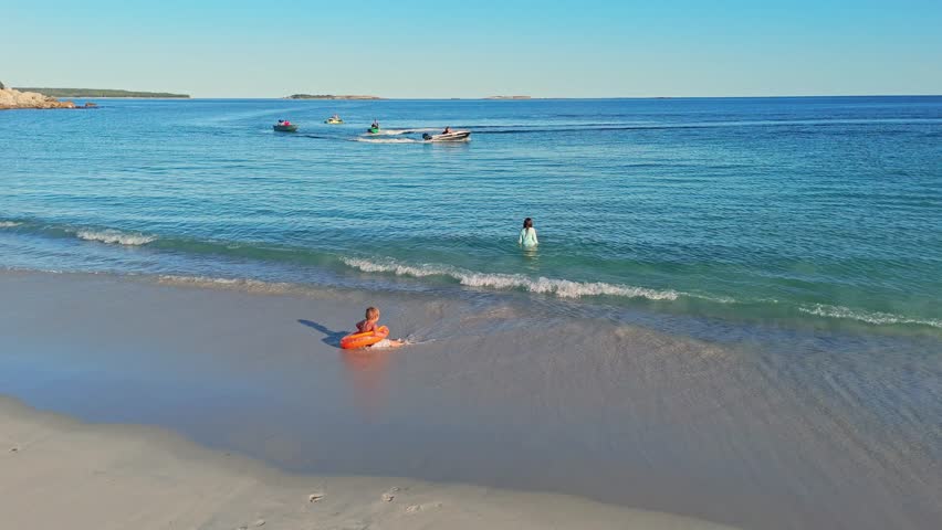 Drone Captures A Man On A Fast Jet Ski Carving Circles In Blue-Green Sea Water, Splashing Foam And Enjoying A Sunny Day Of Freedom, Power, And Summer Energy.