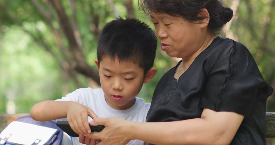 Chinese grandparents and grandchildren looking at and playing with their mobile phones outdoors