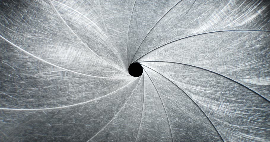 Circular blades of a mechanical iris create a precision opening controlling amount of light entering a camera lens with the opening mechanism controlling the aperture and the depth of field in focus.