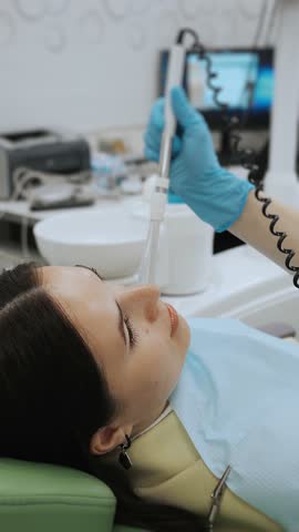Dentist using curing light device during patient treatment in modern dental clinic, vertical medical frame showing oral care procedure under professional equipment