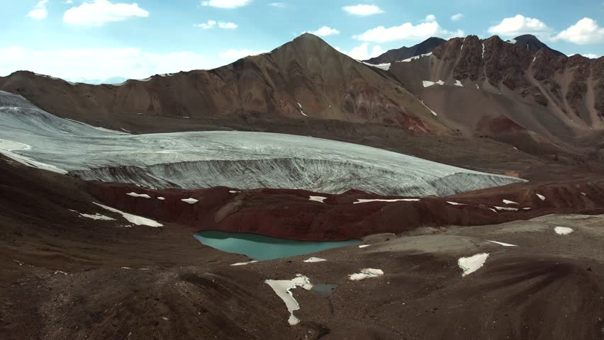 Wide drone panorama of the north side Camp 1 zone of Lenin Peak in Kyrgyzstan, with crevassed ice, serrated ridges, and stark high altitude terrain.