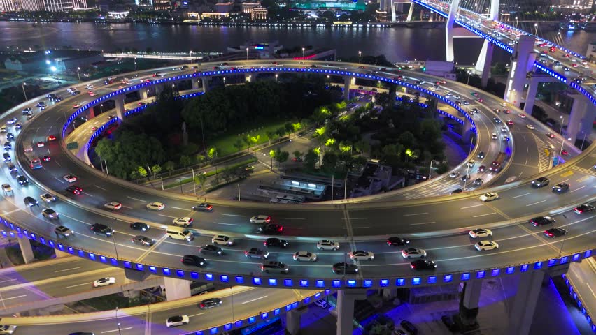 Aerial view of the illuminated Nanpu Bridge interchange with heavy vehicle traffic at night, alongside the Huangpu River in Shanghai, China.