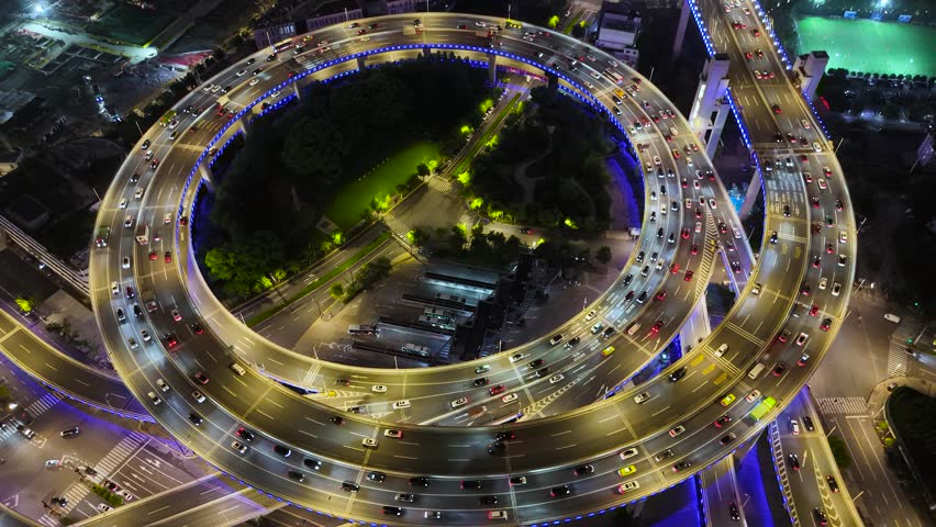 Aerial view of the illuminated spiraling highway interchange, bustling with vehicle traffic at night, showcasing modern urban infrastructure in Shanghai, China.