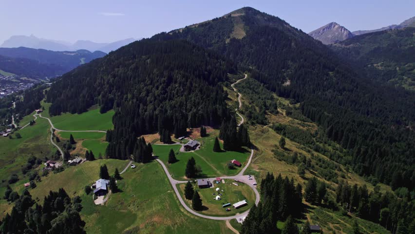 Lush green French Alps tourist destination top of Mont Chery slopes near Les Gets village with rocky mountain tops behind against a clear blue sky