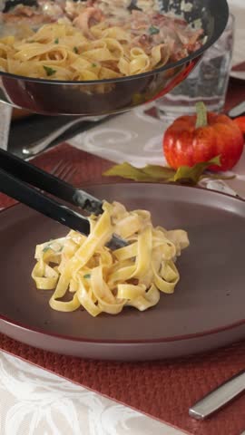 Anonymous person put tagliatelle with sauce and mushrooms from pan onto plate. Food and cooking at home in kitchen. Healthy eating. Table setting. 