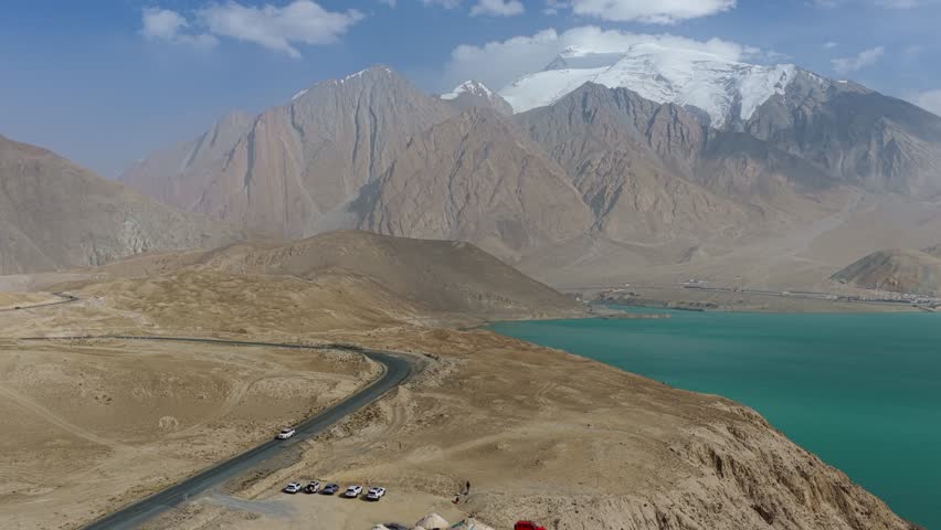 Aerial view of the serene Baisha Lake contrasting with the stark mountains and winding roads under a clear sky, Baisha Lake, Xinjiang, China.