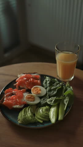 A nutritious breakfast plate with smoked salmon, avocado slices, boiled eggs, fresh greens, and a glass of orange juice on a wooden table. Perfect for illustrating healthy eating, balanced diet, or