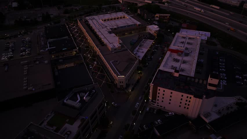 Aerial descend to Bottleworks District rooftops and roads under warm purple sunset light, Indianapolis Indiana