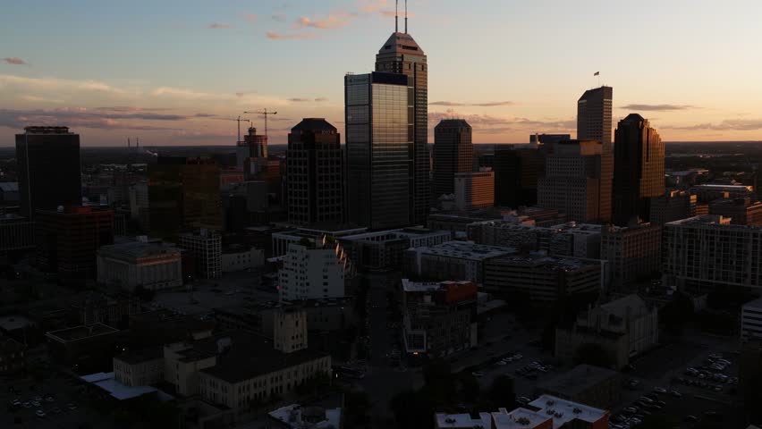 Drone ascends above Massachusetts Avenue. Downtown Indianapolis skyline at sunset, reveal city skyscrapers and landmarks in warm summer light.