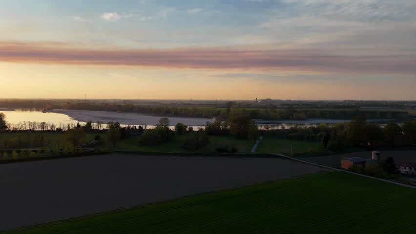 A drone shot captures the River Po winding past the Maginot and Bodri fields under a stretched stratocumulus cloud, painting soft layers across the sky during golden sunset over farmland, slow motion