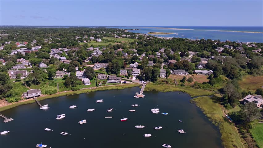 Aerial view of boats in the harbor surrounded by houses and greenery, with the ocean beyond, a beautiful palette of blue and green. Chatham, Cape Cod, Massachusetts, USA.