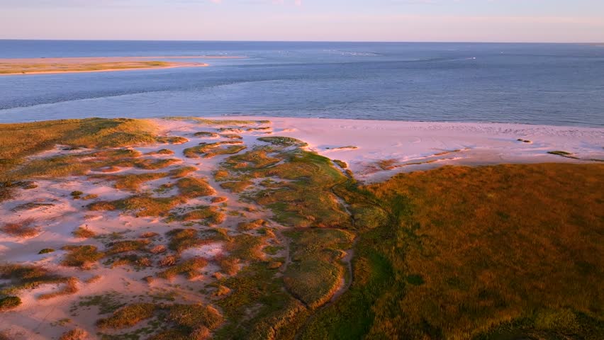 Aerial view of the tranquil beach meeting the vast ocean, where the sandy shore blends with the sea, creating a serene coastal scene at sunset. Chatham, Cape Cod, USA.