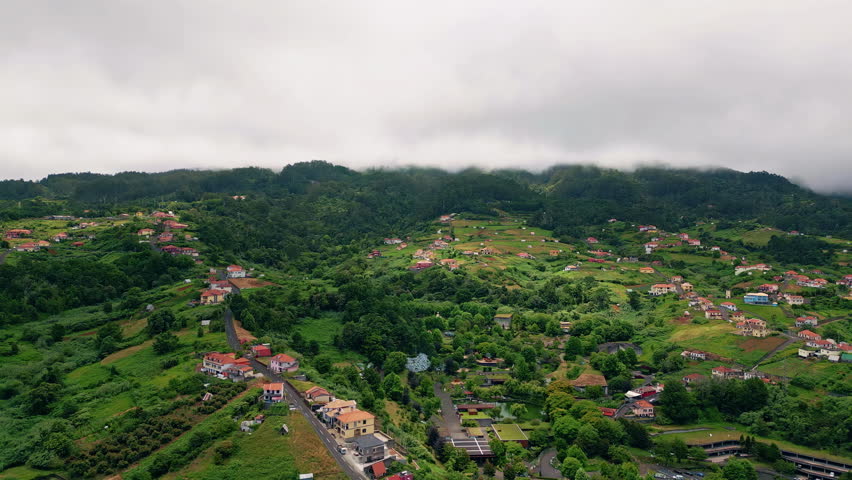 Rural landscape under cloudy sky aerial view. Cozy small village placed in lush greenery gloomy day. Countryside buildings with red rooftops hiding in green nature vegetations. Beautiful scenery.