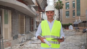 Male engineer in helmet and vest holds blueprints and tablet at construction site smiling at camera - Powered by Shutterstock - Get 15% off with code: PIKWIZARD15